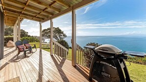 Un espace extérieur abrité, avec vue sur l’océan, comprenant un barbecue et des sièges.
