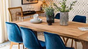 Zona pranzo con tavolo in legno, sedie in velluto blu, lampada a sospensione intrecciata e tappeto decorato.