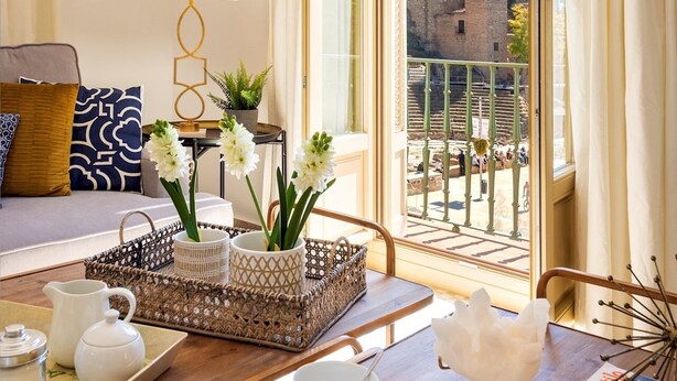 Una stanza luminosa con un balcone, un divano, un tavolo con un vassoio di te e vista su un edificio storico.