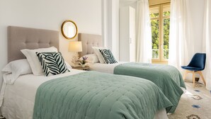 Camera d'albergo con due letti, uno specchio tondo, un comodino con lampada e vista sul verde dalla finestra.