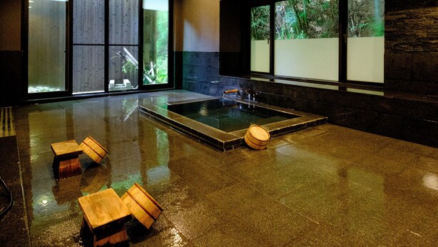 A modern spa room with a large hot tub, wooden stools, and large windows offering views of the outdoors. - Misasaonsen Kouraku (Misasa)