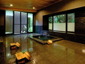 A modern spa room with a large hot tub, wooden stools, and large windows offering views of the outdoors. - Misasaonsen Kouraku (Misasa)