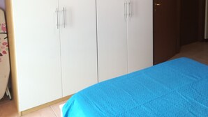 A bedroom with a large wardrobe, a bed with a blue bedspread, and an air conditioning unit on the wall. - Two-room apartment for rent (Ravenna)