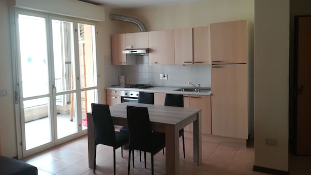 A modern kitchen with a dining area, featuring a large window, sliding doors, and a built-in stove. - Two-room apartment for rent (Ravenna)