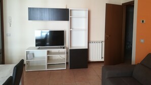 A living room with a TV on a stand, a sofa, a white cabinet, and a radiator. - Two-room apartment for rent (Ravenna)