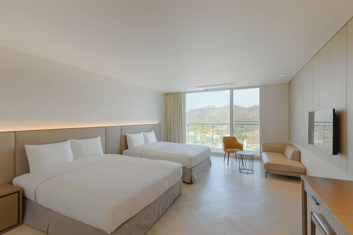 Una habitación de hotel moderna con dos camas, un sofá, un televisor y un balcón con vistas.