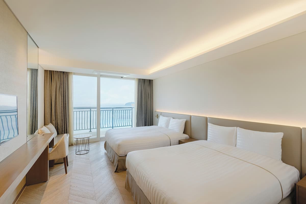 Habitación de hotel con dos camas, un escritorio y vista al mar.