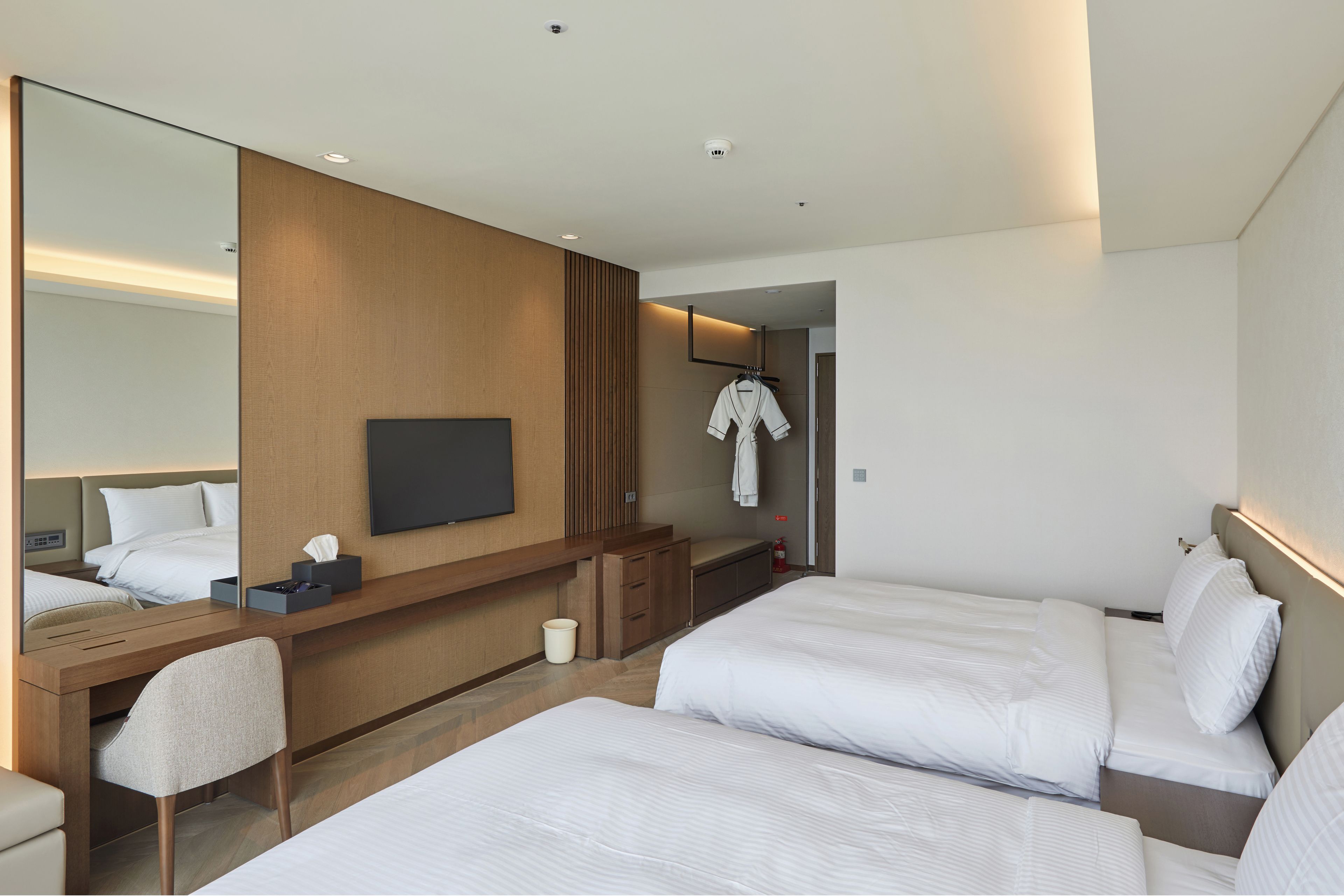 Habitación de hotel con dos camas, un escritorio, una silla, un televisor y un espejo.