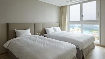 A hotel room with two beds, a large window with a view of buildings and hills, and a ceiling light fixture.