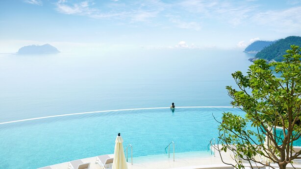 A clear view of an infinity pool with a person swimming, surrounded by lounge chairs and a tree. - Sol Beach Jindo (Jindo)