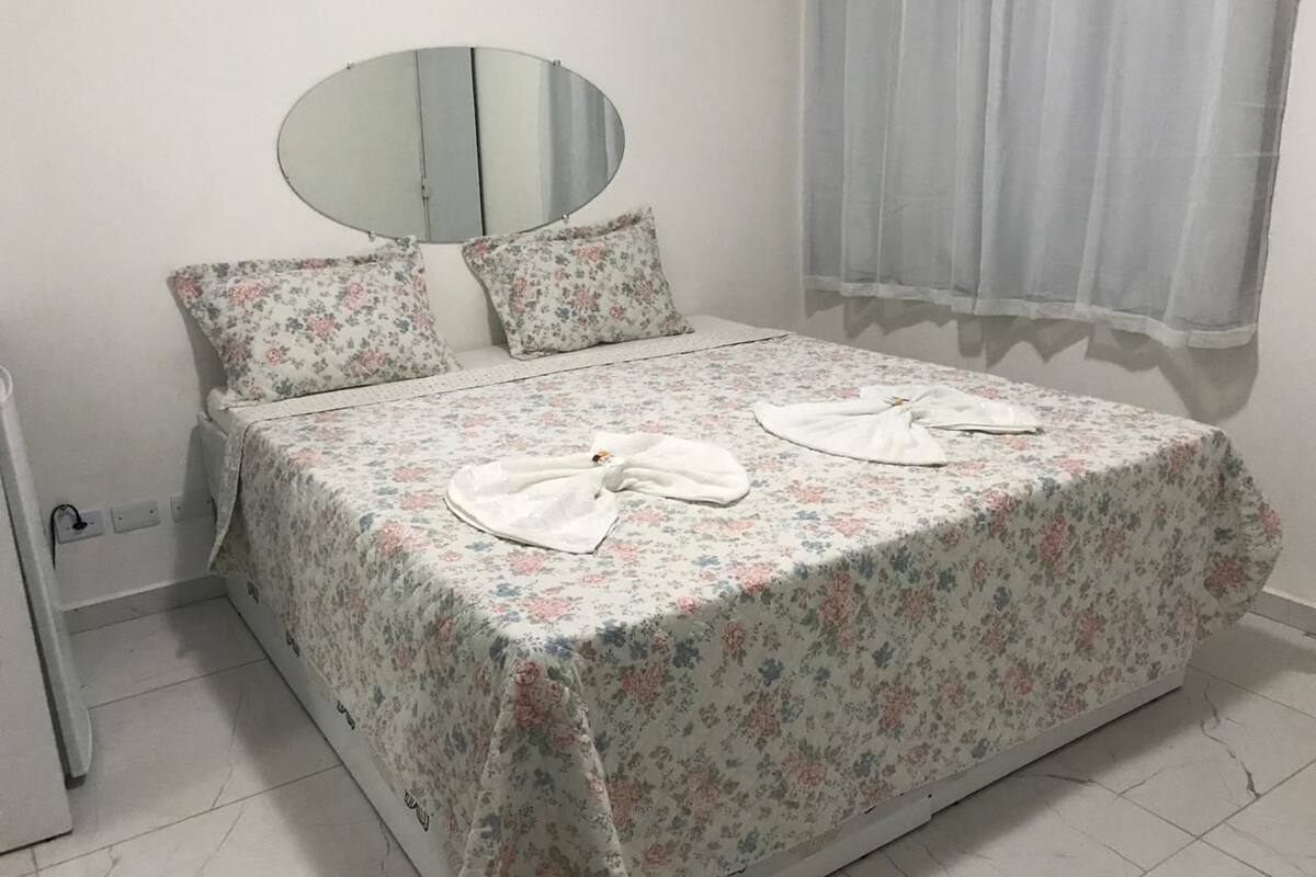 Ein Schlafzimmer mit einem Bett, einem runden Spiegel und einem Fenster mit Vorhängen.