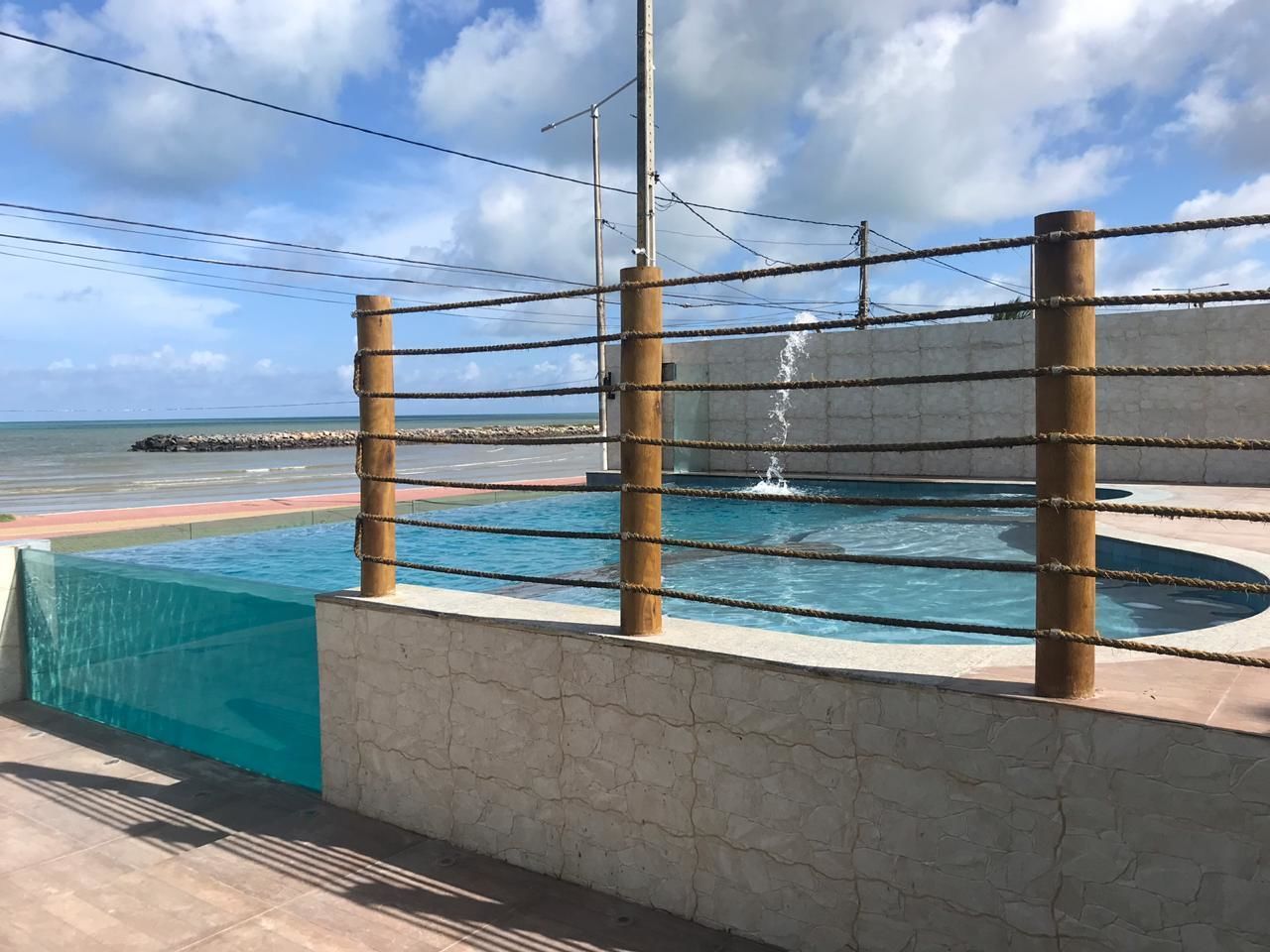 Uma área de piscina com uma barreira de corda, um muro de pedra e vista para o oceano.