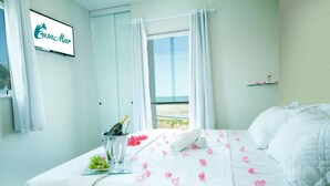 A hotel room with a bed, a minibar, a window with curtains, and a view of the beach. - CasaMar Pousada (Paulista)