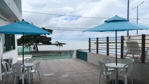 An outdoor patio with tables and chairs, a pool, and umbrellas. - CasaMar Pousada (Paulista)