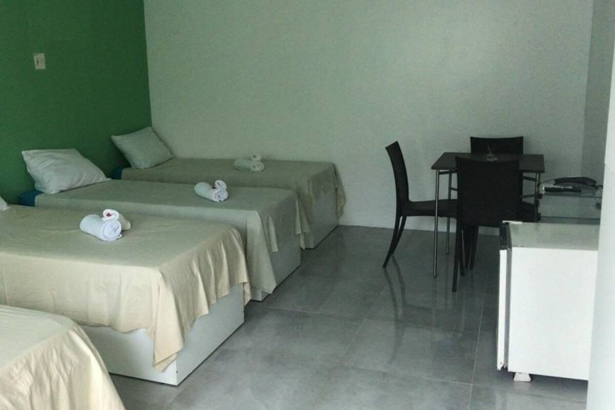 Ein Hotelzimmer mit drei Einzelbetten, einem Schreibtisch und einem Stuhl.