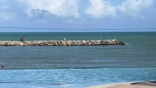 A pool area with a view of the ocean and a rocky breakwater. - CasaMar Pousada (Paulista)