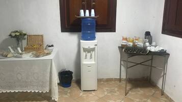 Uma pequena cozinha compacta com um bebedouro, uma mesa com alimentos e um espaço para café.