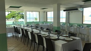 A dining area with tables set for service, large windows with a view of the sea, and a tiled floor. - CasaMar Pousada (Paulista)