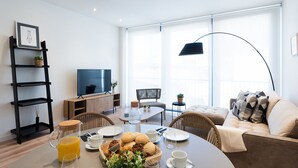 Una sala moderna con comedor, televisor y un ventanal grande.