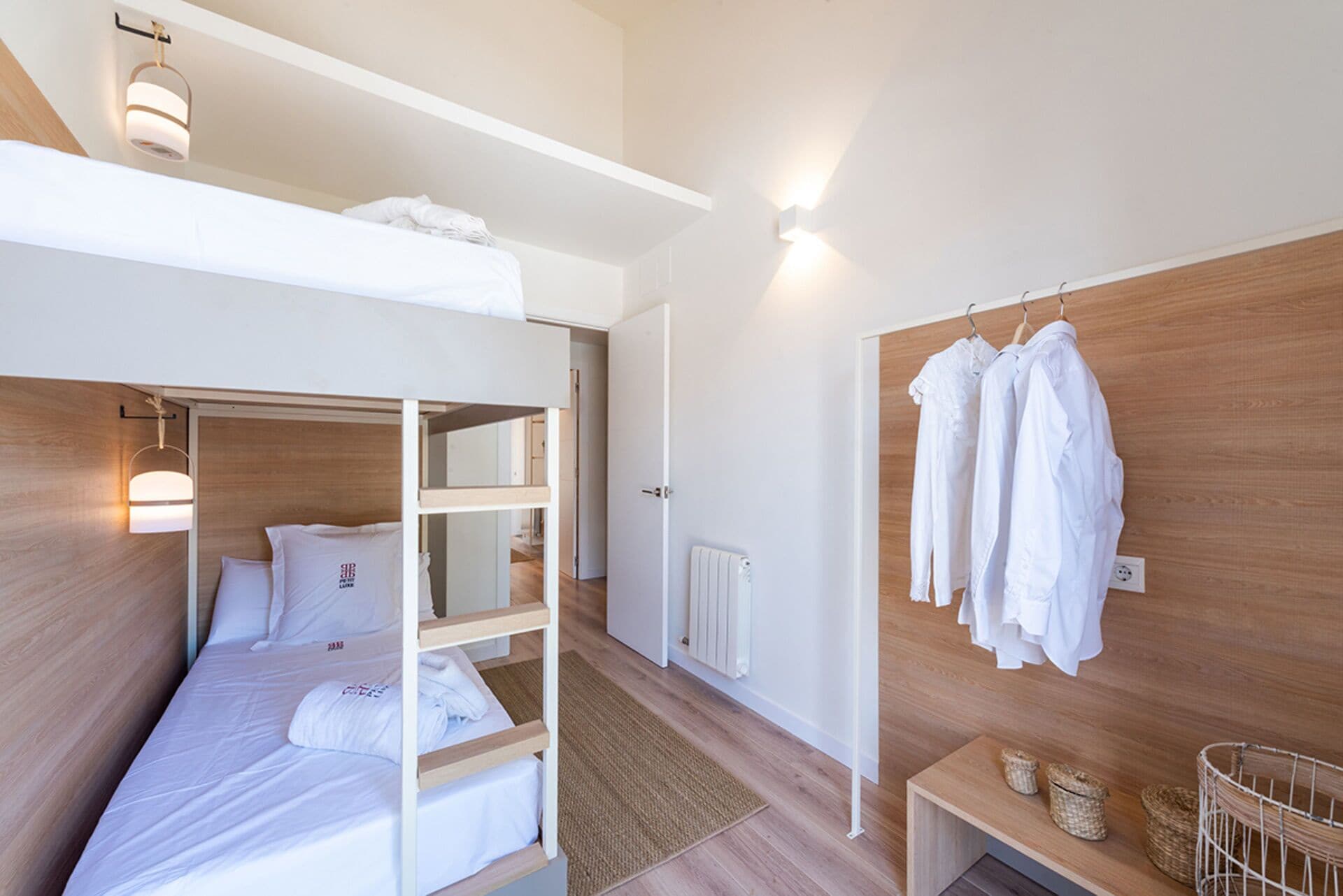 A bunk bed room with a wooden headboard, a bedside table, and a wall-mounted drying rack.