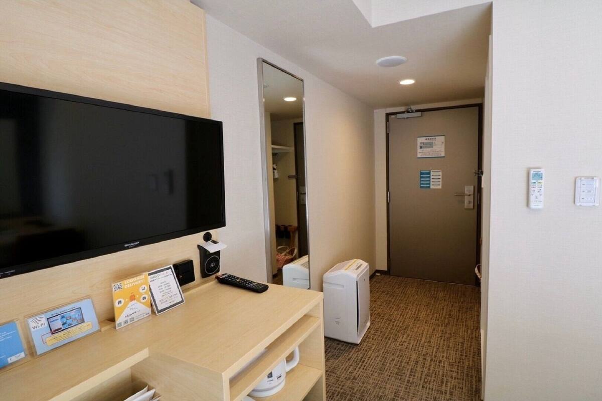 Habitación de hotel con televisión de pantalla plana, un escritorio con control remoto, un calentador pequeño y una puerta con un letrero.