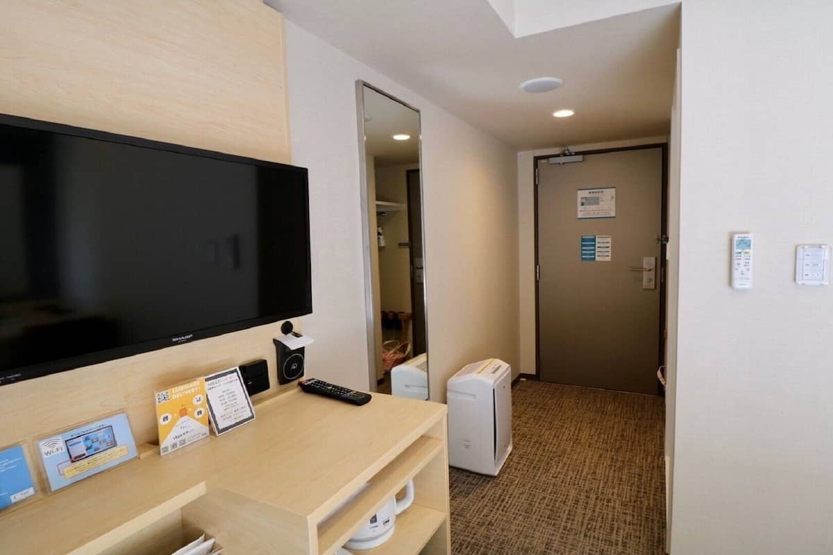 Ein Hotelzimmer mit Flachbildfernseher, Schreibtisch mit Fernbedienung, kleinem Heizgerät und einer Tür mit einem Hinweisschild.