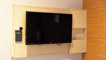 A flat-screen TV mounted on a wooden wall unit with a control panel and a small storage compartment.