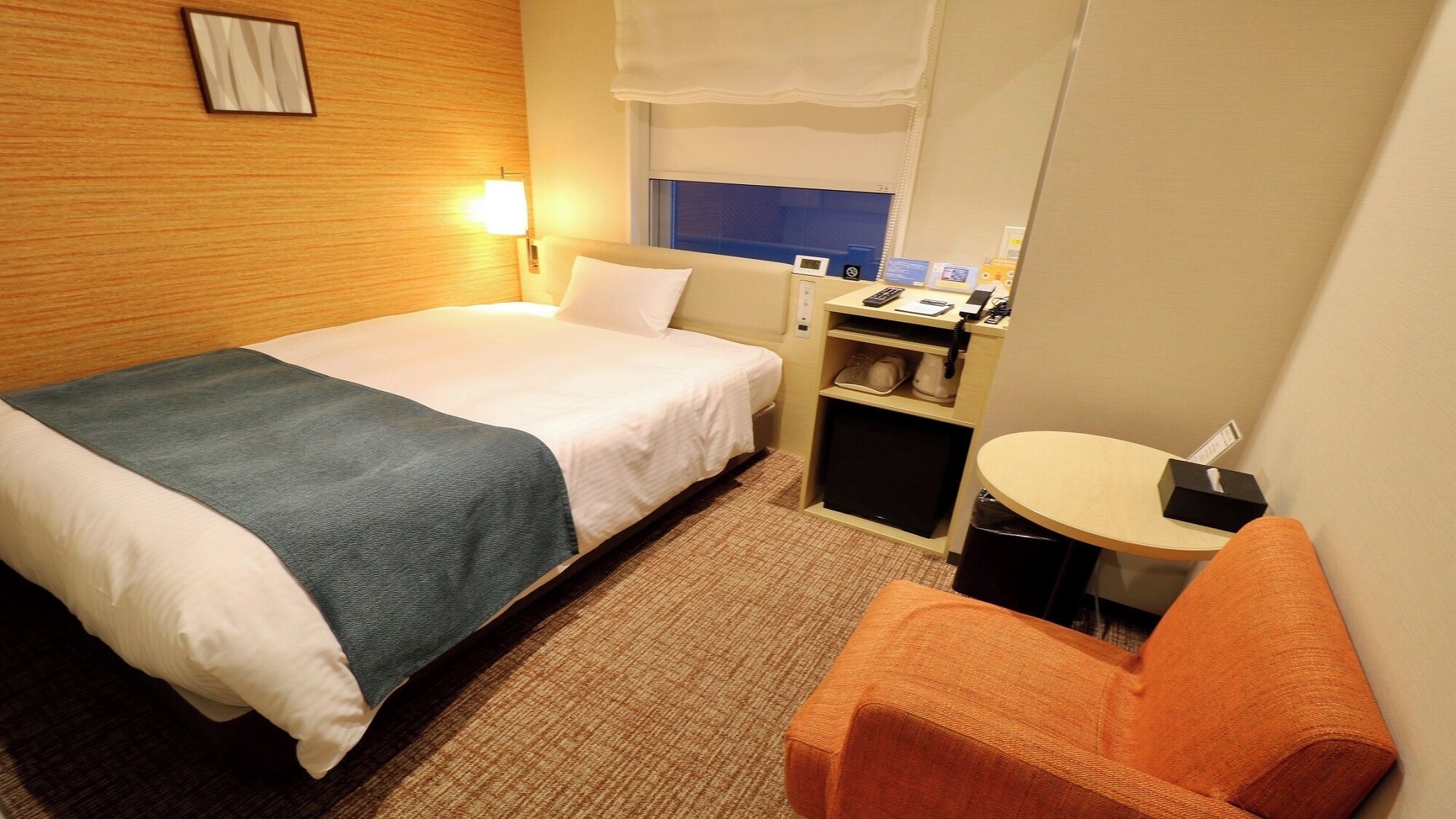 A hotel room with a bed, a desk, a chair, and a small table.