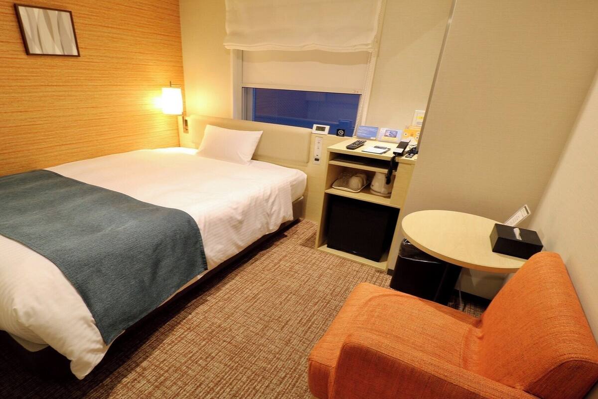 Una habitación de hotel con cama, escritorio, silla y una mesita.