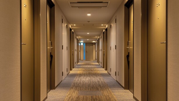 A long, narrow hotel corridor with doors on both sides, a carpeted floor, and a blue door at the end. - Keikyu EX Inn Akihabara (Tokyo)