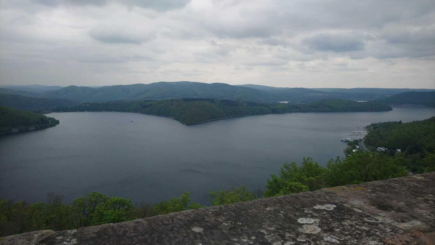 A panoramic view of a large lake surrounded by hills and a stone wall in the foreground.