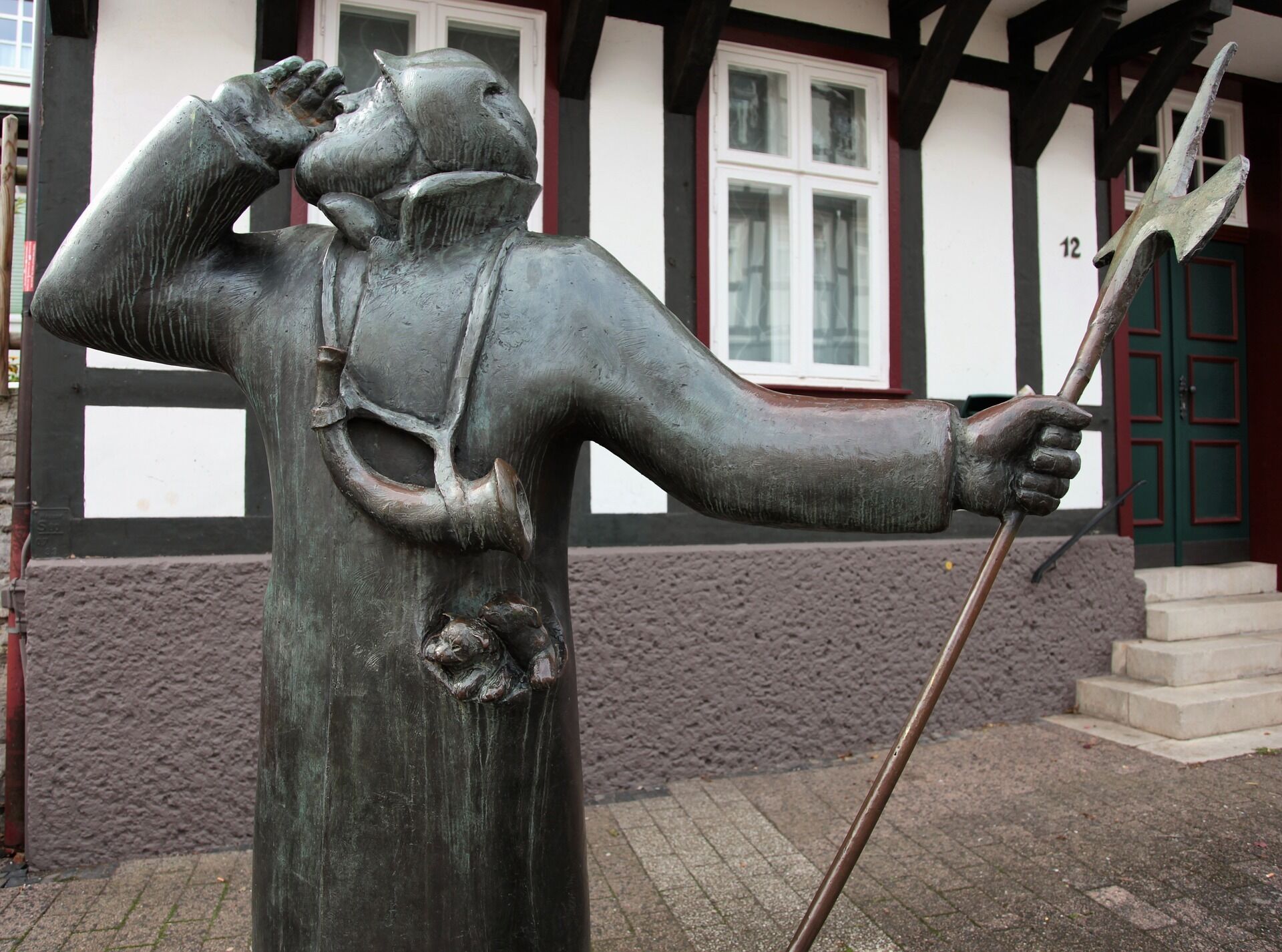 Eine Statue eines Mannes mit Stab und Schild, vor einem Gebäude mit der Nummer 12 an der Tür.