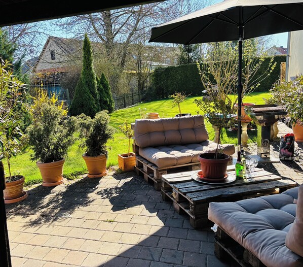 A patio area with a cushioned seating arrangement, potted plants, and a barbecue grill.