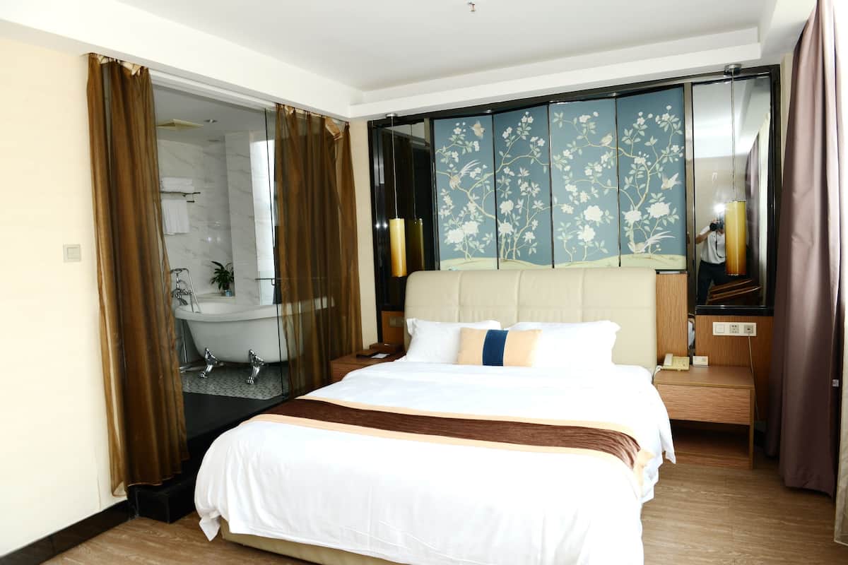 Habitación de hotel con una cama grande, baño con bañera y puerta corrediza con papel tapiz floral.