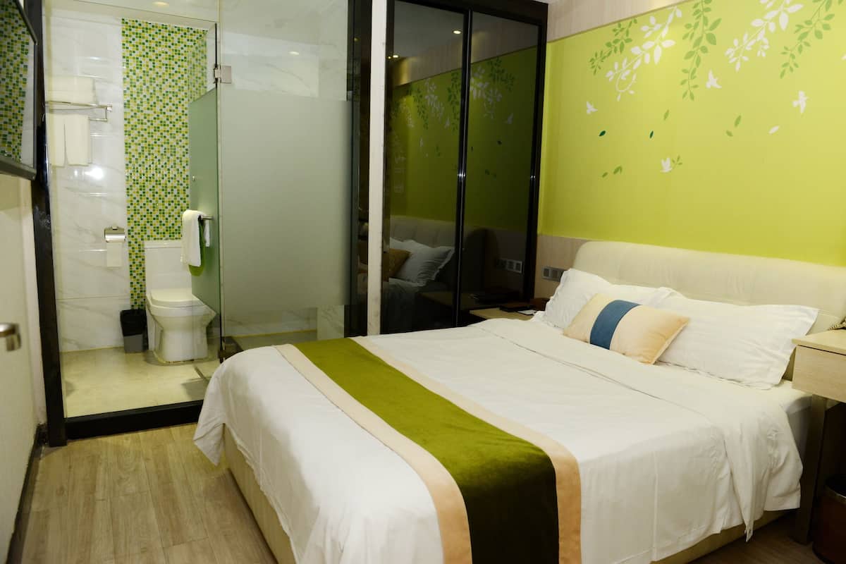 Habitación de hotel con cama, baño y pared verde decorada con motivos florales.