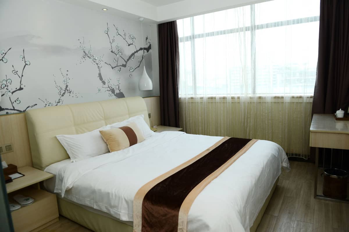 Habitación de hotel con una cama grande, una mesita de noche, un escritorio y una ventana con cortinas.