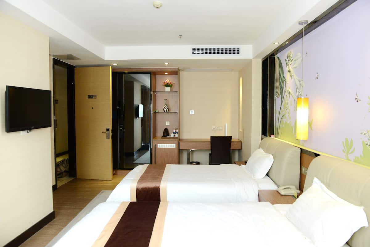 Habitación de hotel con dos camas, un escritorio, una silla, un televisor y la puerta del baño.