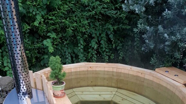 A wooden hot tub with a metal structure on top, surrounded by a wooden deck and greenery. - Sommerhof in the beautiful Havelland (Märkisch Luch OTBuschow)