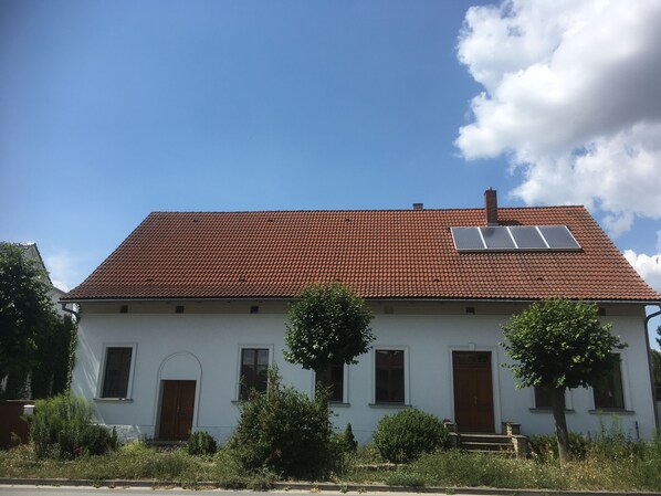 A white building with a red-tiled roof, a wooden door, and a small window.