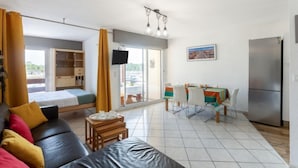 A modern living room with a sofa, a dining area with a table and chairs, a kitchen with a refrigerator, and a large window with curtains. - le Grand Foc by Interhome (Capbreton)