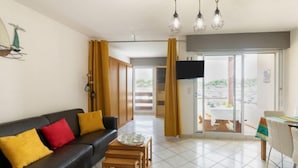A modern living room with a black sofa, yellow cushions, a wooden coffee table, and a dining area with a white table and chairs. - le Grand Foc by Interhome (Capbreton)