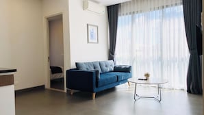 Ein modernes Wohnzimmer mit einem blauen Sofa, einem kleinen runden Tisch und einem großen Fenster mit transparenten Vorhängen.
