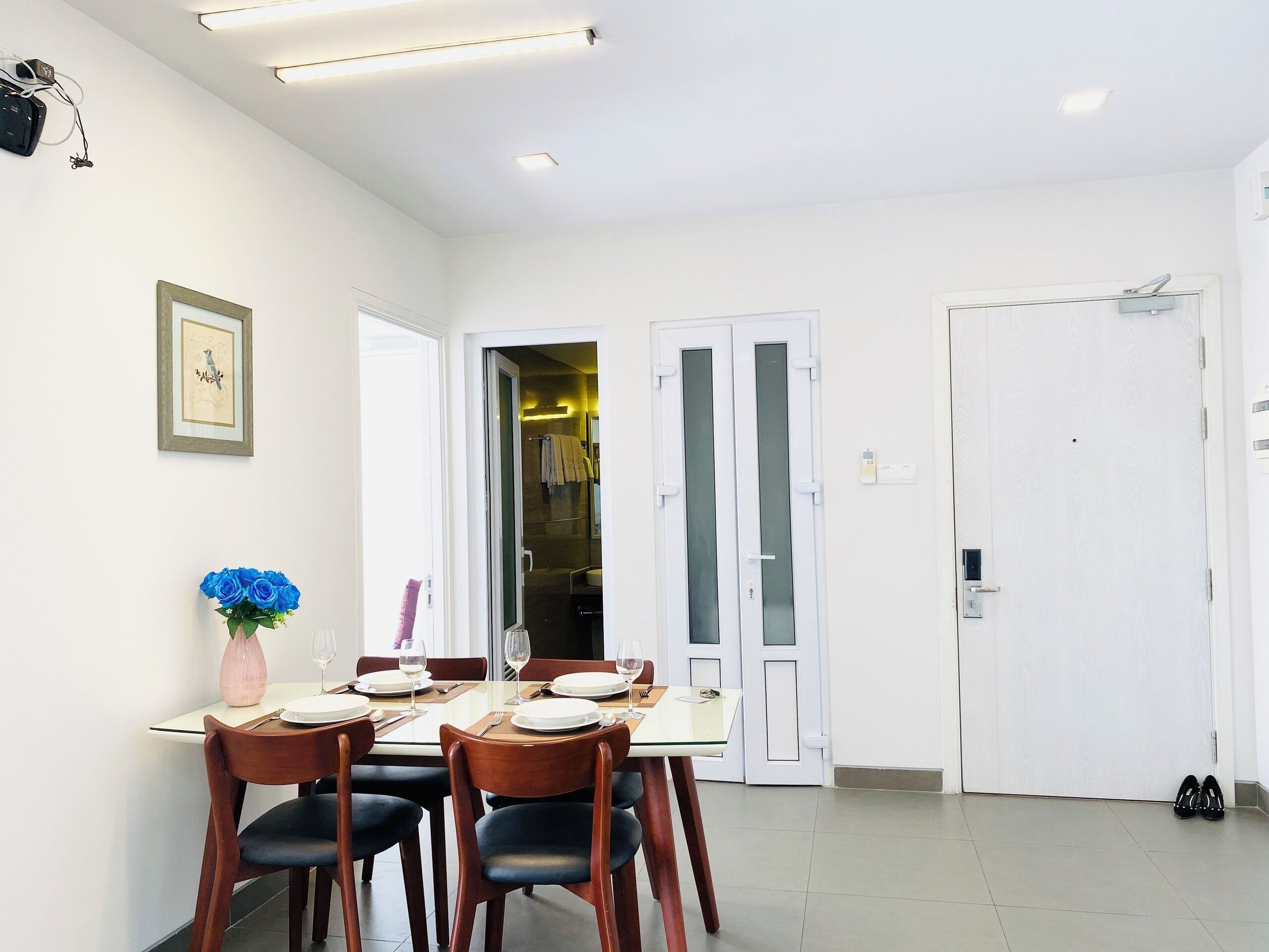 A dining area with a table set for four, a vase of blue flowers, and a framed picture on the wall.