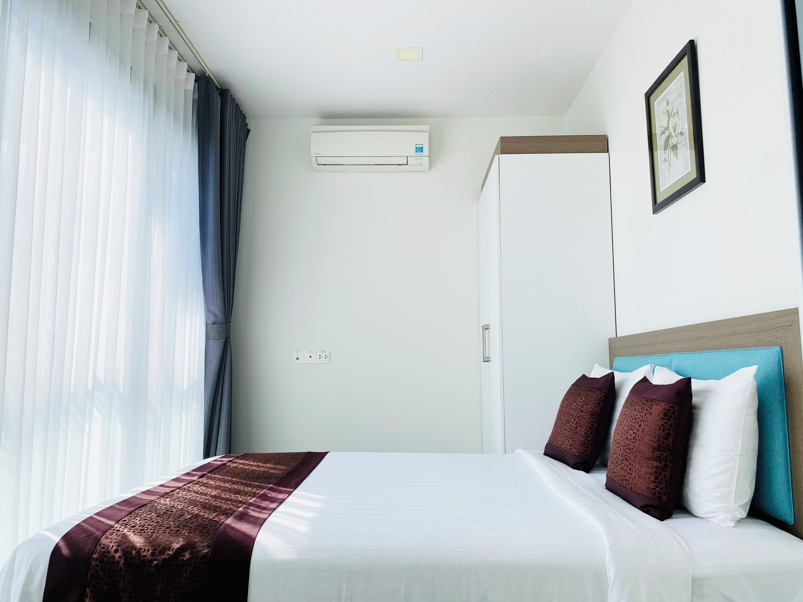 A hotel room with a bed, a wardrobe, an air conditioning unit, and a framed picture on the wall.