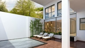 Ein moderner Außenbereich mit Pool, Liegestühlen und einer Glaswand mit Blick auf einen Garten.