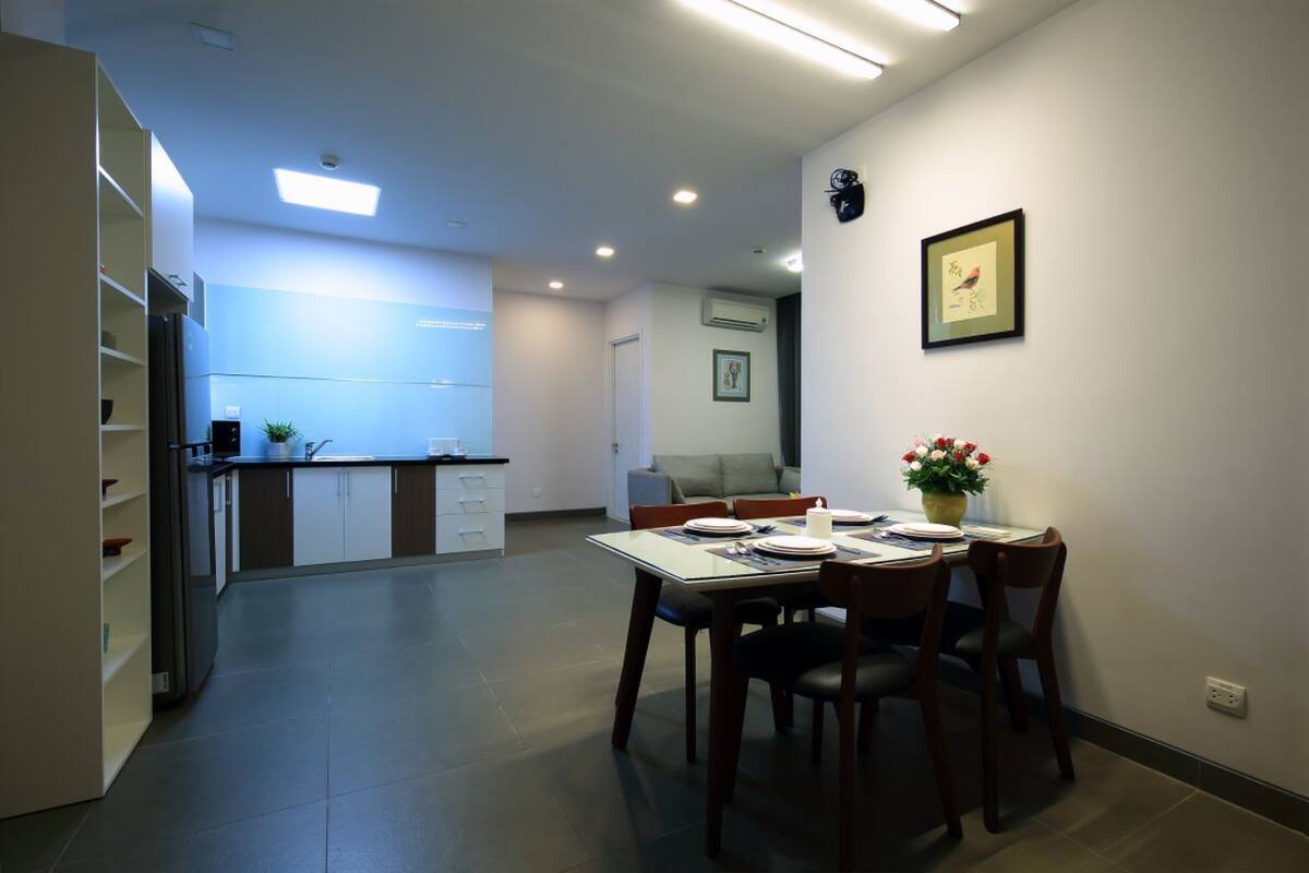 A modern kitchen with a dining area, featuring a table set for four, a refrigerator, and a sink.