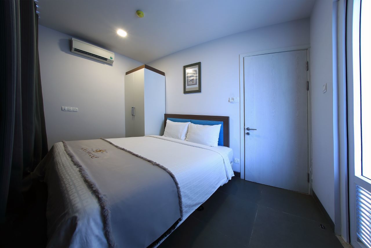 A hotel room with a bed, an air conditioning unit, a door, and a window.