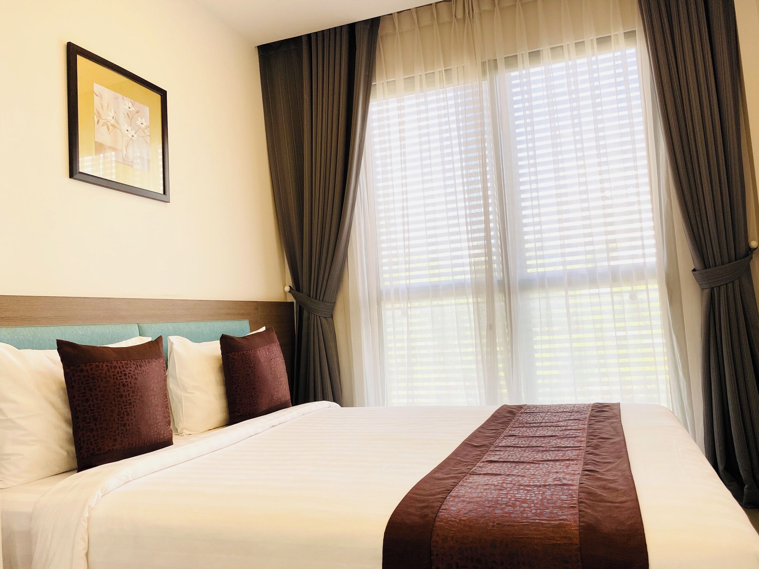 A hotel room with a large bed, a headboard, and a window with curtains.