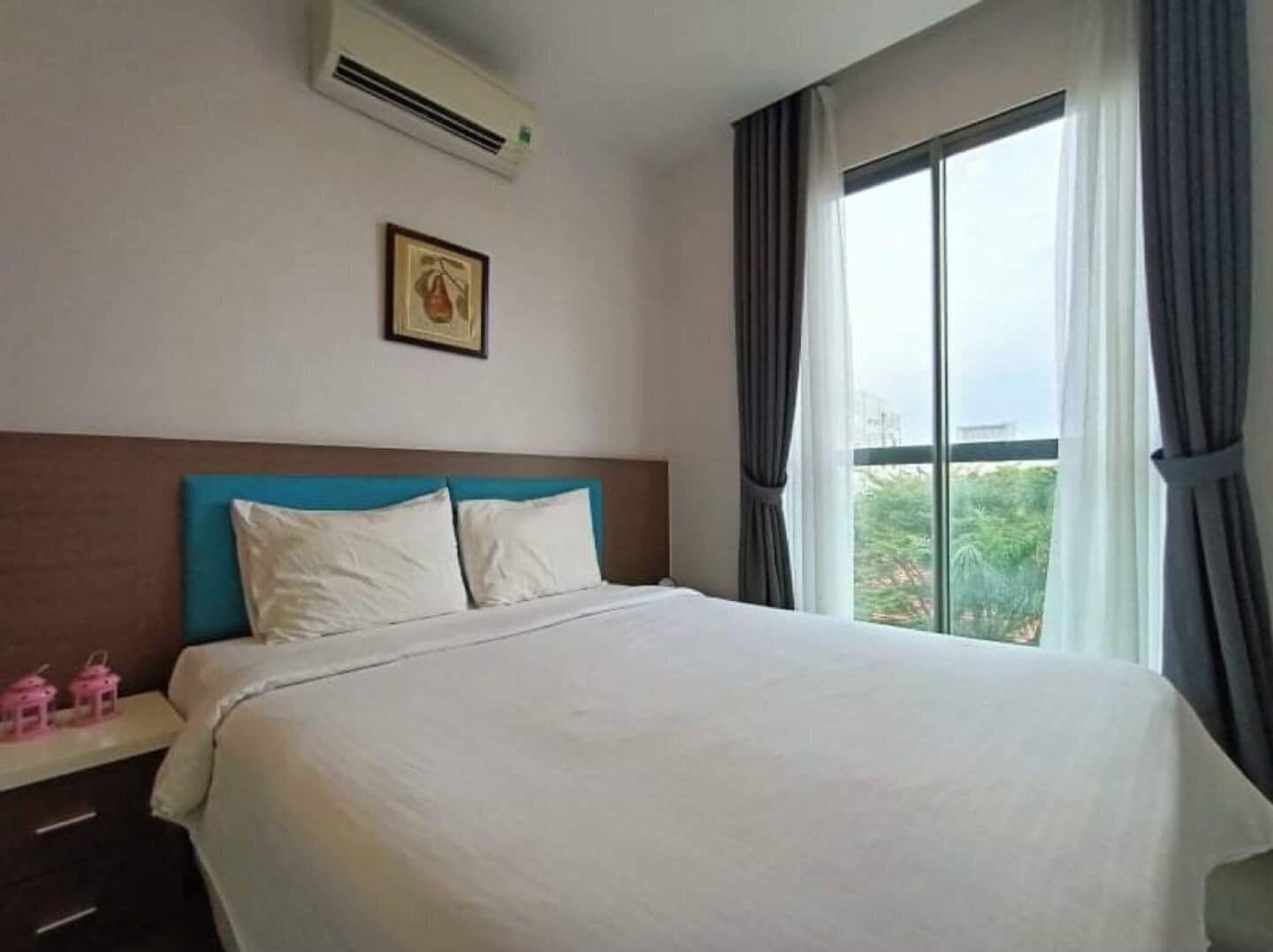 A hotel room with a bed, a nightstand, a framed picture on the wall, and a window with curtains.