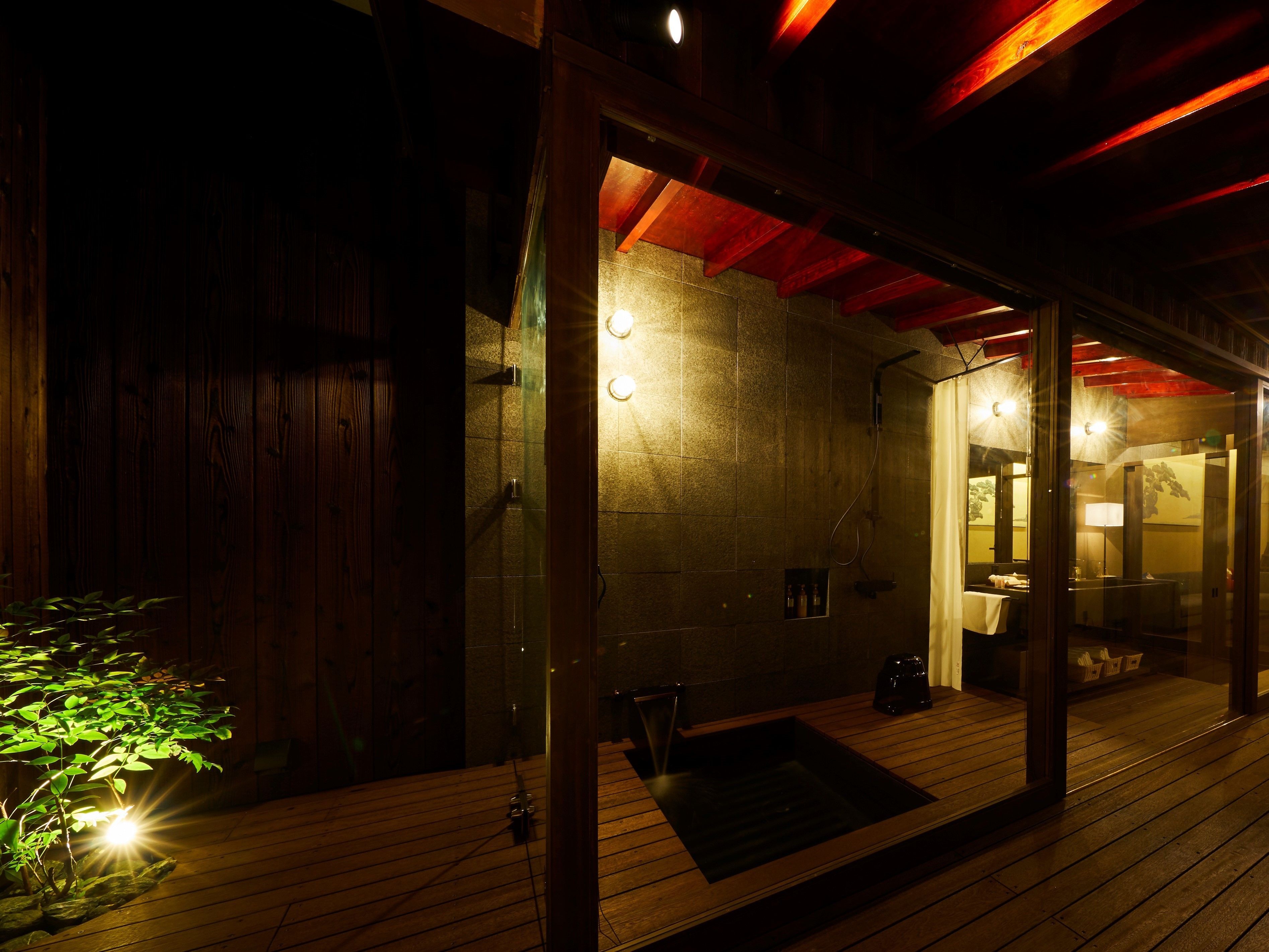 Une terrasse en bois avec un espace sauna fermé par des parois de verre, des murs en pierre et un plafond rouge.